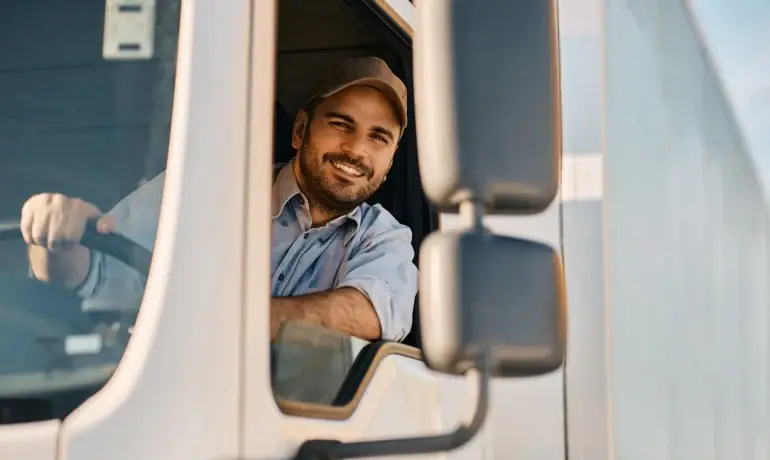 Happy professional truck driver driving his truck and looking at camera